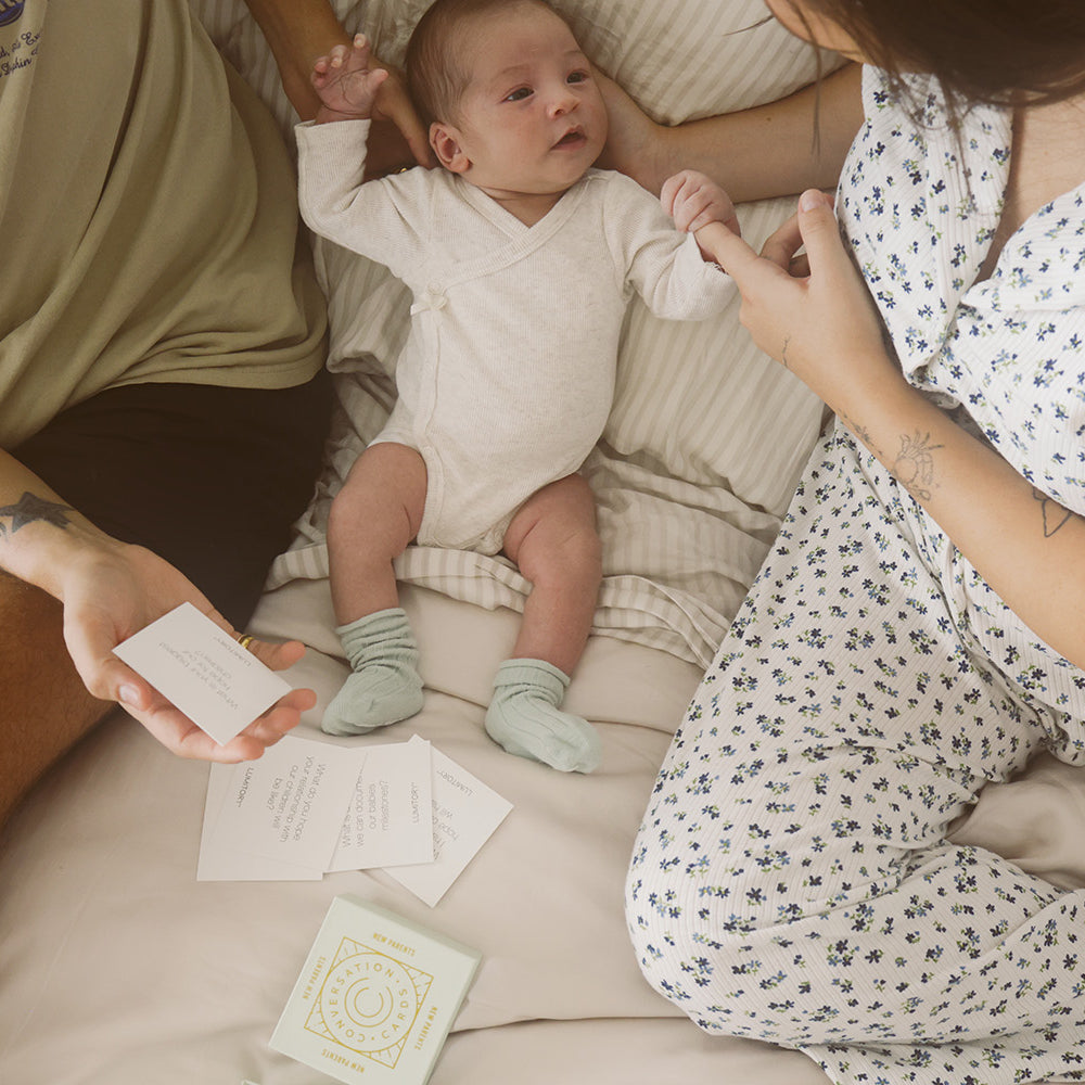 Young parents holding baby on the couch reading conversation cards together.